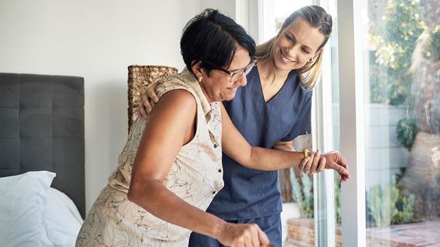 A woman gets help from her caregiver to stand up in her home. 
