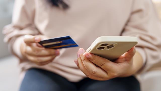 A woman used a smartphone with one hand and holds a credit card in her other. 