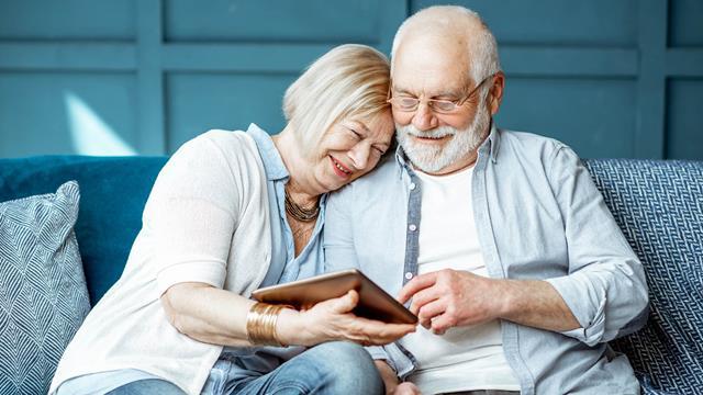 A couple sits close on their sofa and uses a tablet.