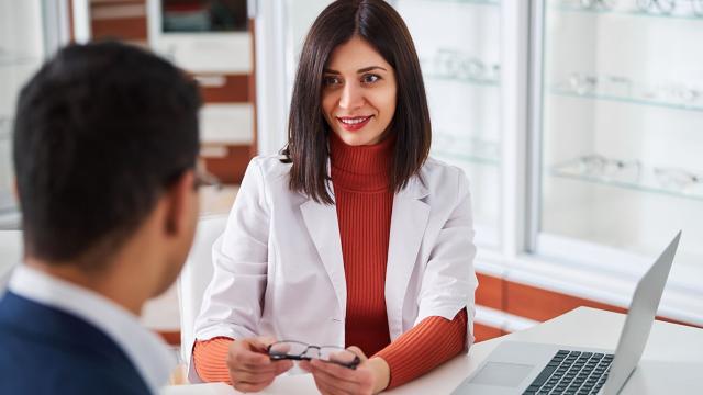 Eye doctor holding glasses talks with a patient.