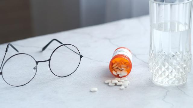 A pair of eyeglasses on a counter next to a bottle of prescription pills.