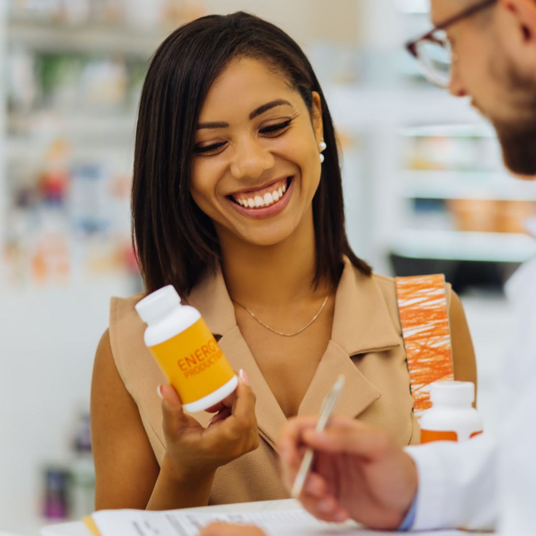 Woman at a pharmacy counter smiling and holding a bottle of pills.