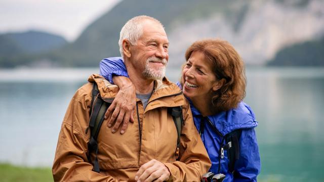 A man smiles as his wife talks to him on a hike. 