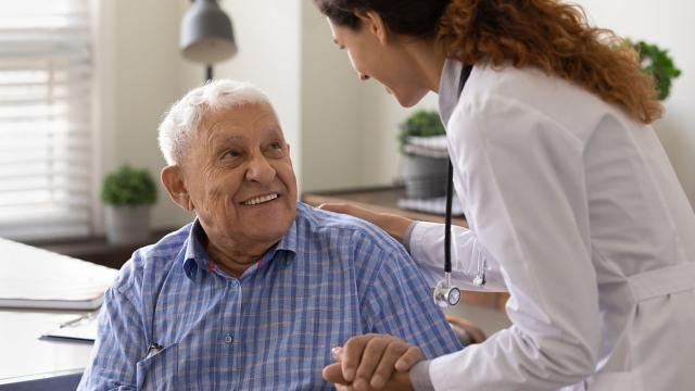 A man smiles up at the provider who holds his hand. 