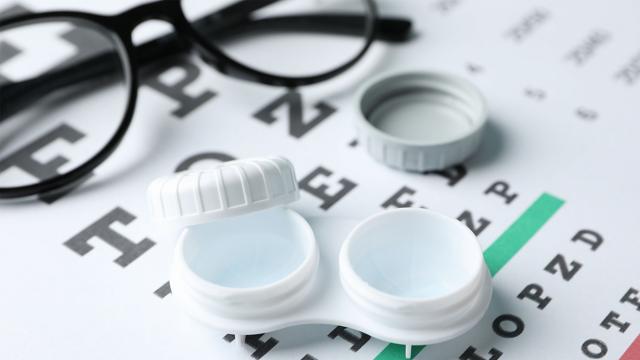 An open contact case lies next to a pair of glasses and an eye chart.