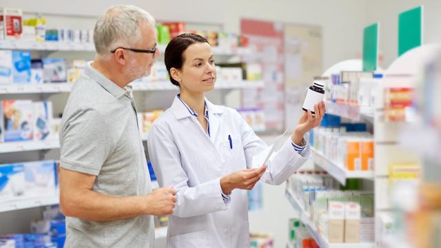 A man consults with a pharmacist near medicine shelves. 