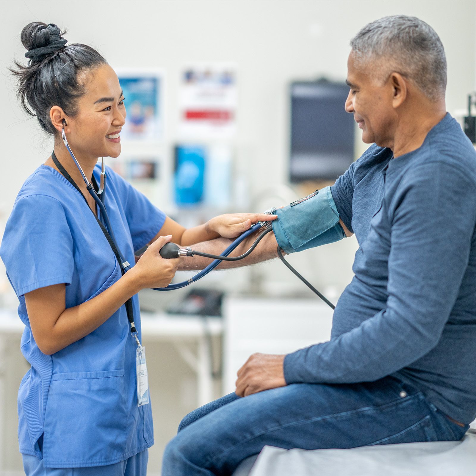 Senior sits on exam table as nurse takes his blood pressure.
