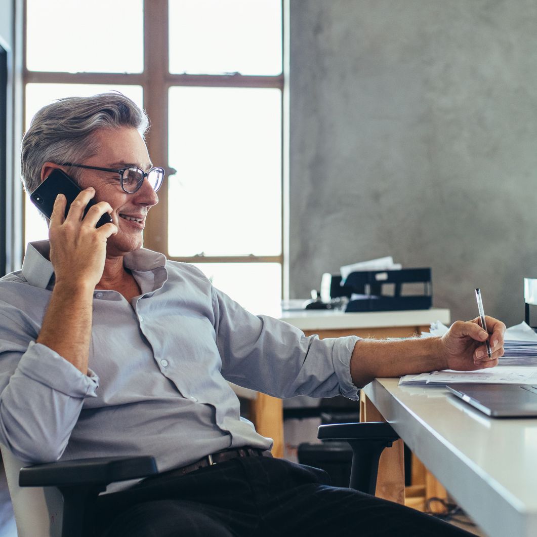 A man smiles as he takes notes while on a phone call.