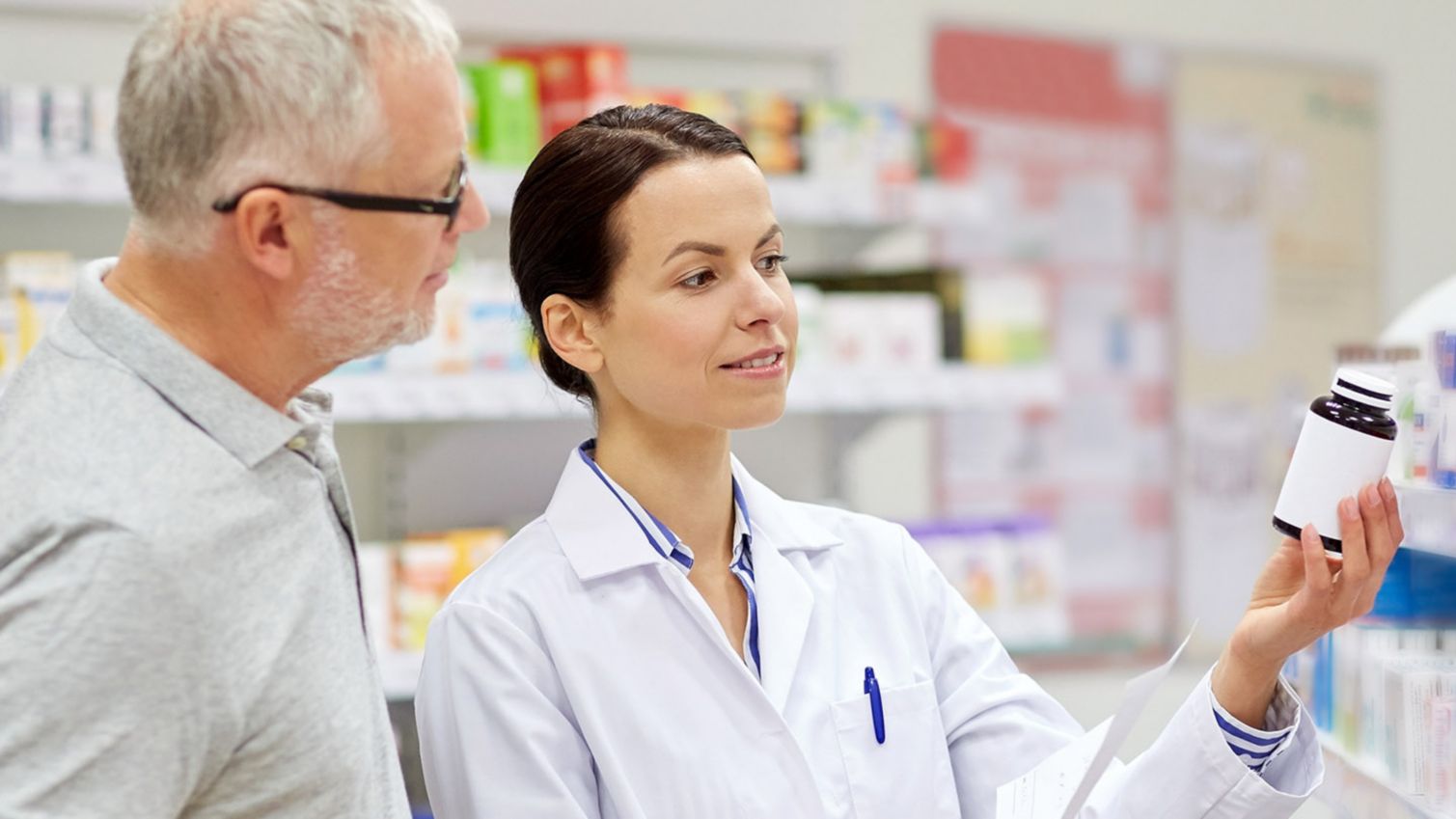 A pharmacist explains the information on a prescription bottle to a man. 