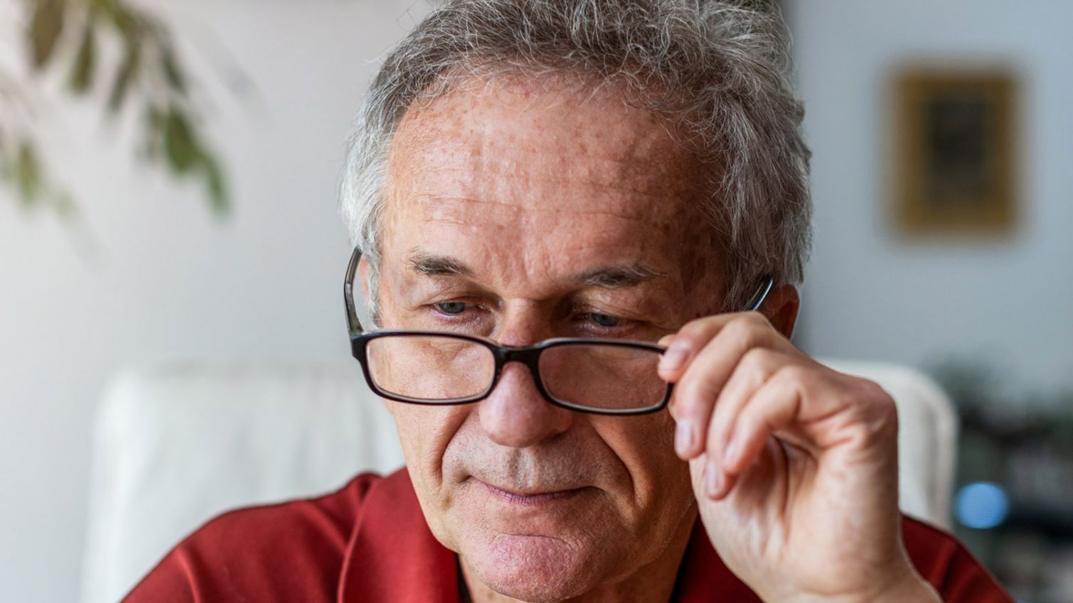 A man adjusts his glasses while reading a prescription label. 