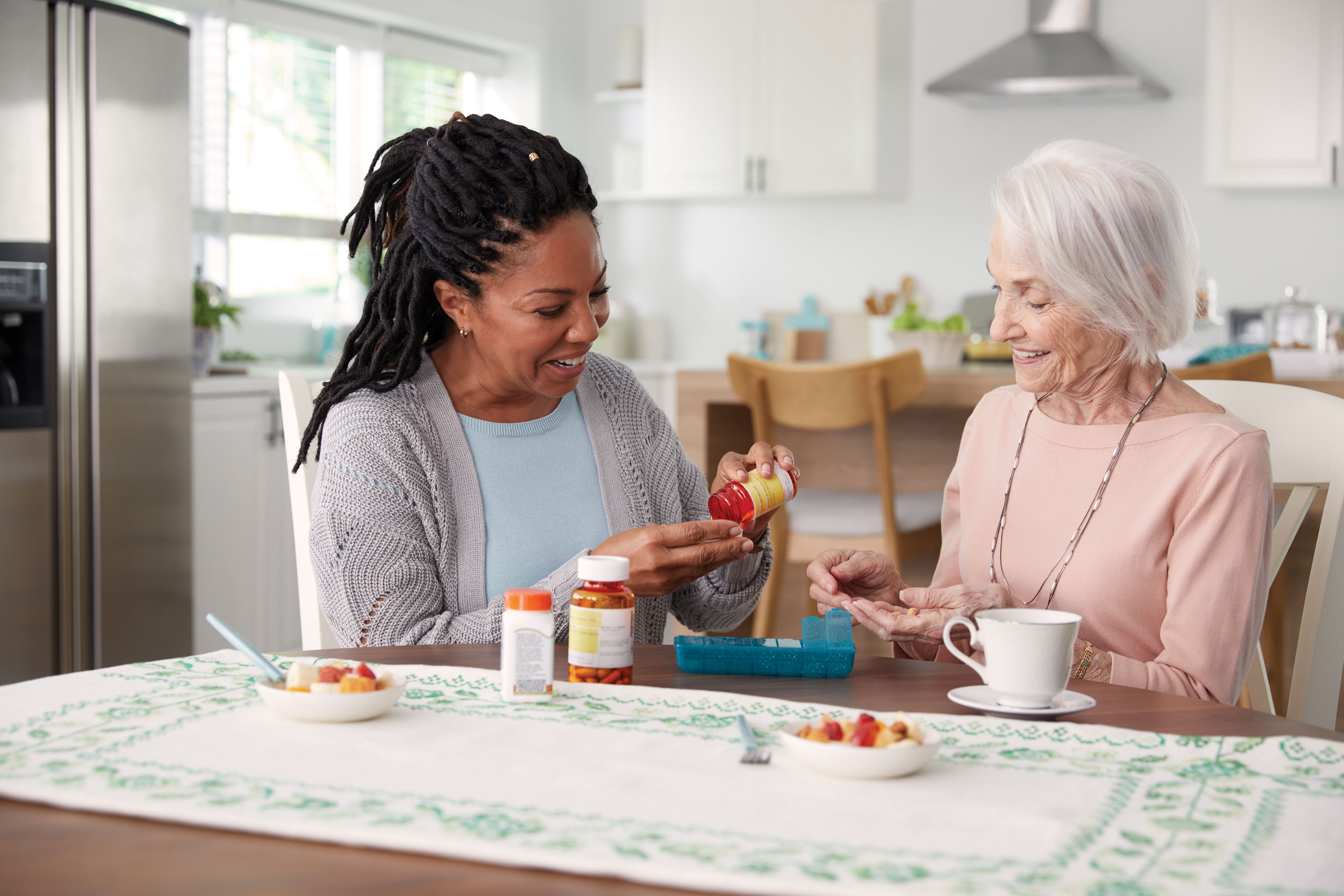 Caregiver helping member sort pills at dining table in kitchen