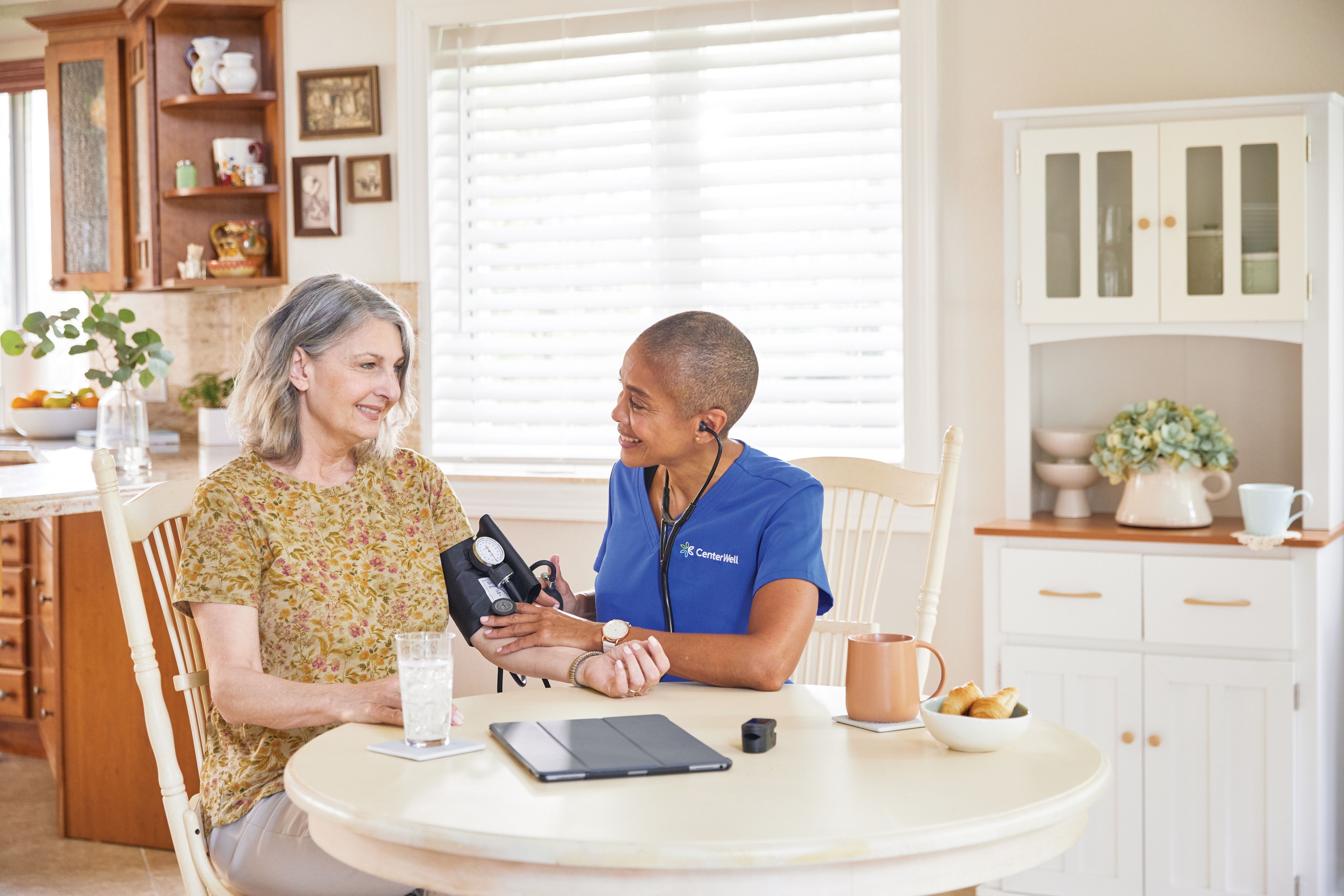 RN checking senior female patients vitals including heart rate at kitchen table in her home.