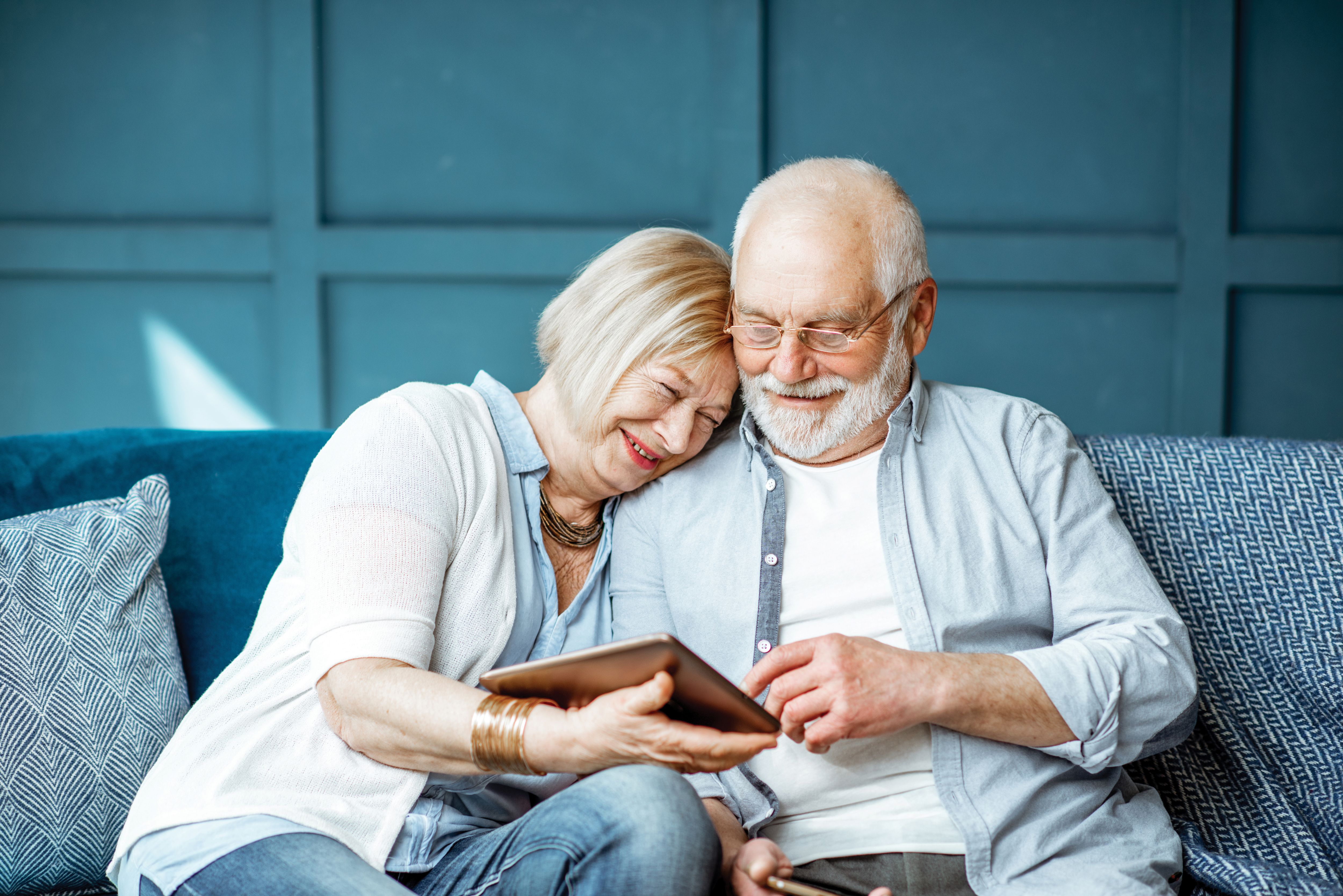 Senior couple dressed casually using digital tablet while sitting together on their couch at home