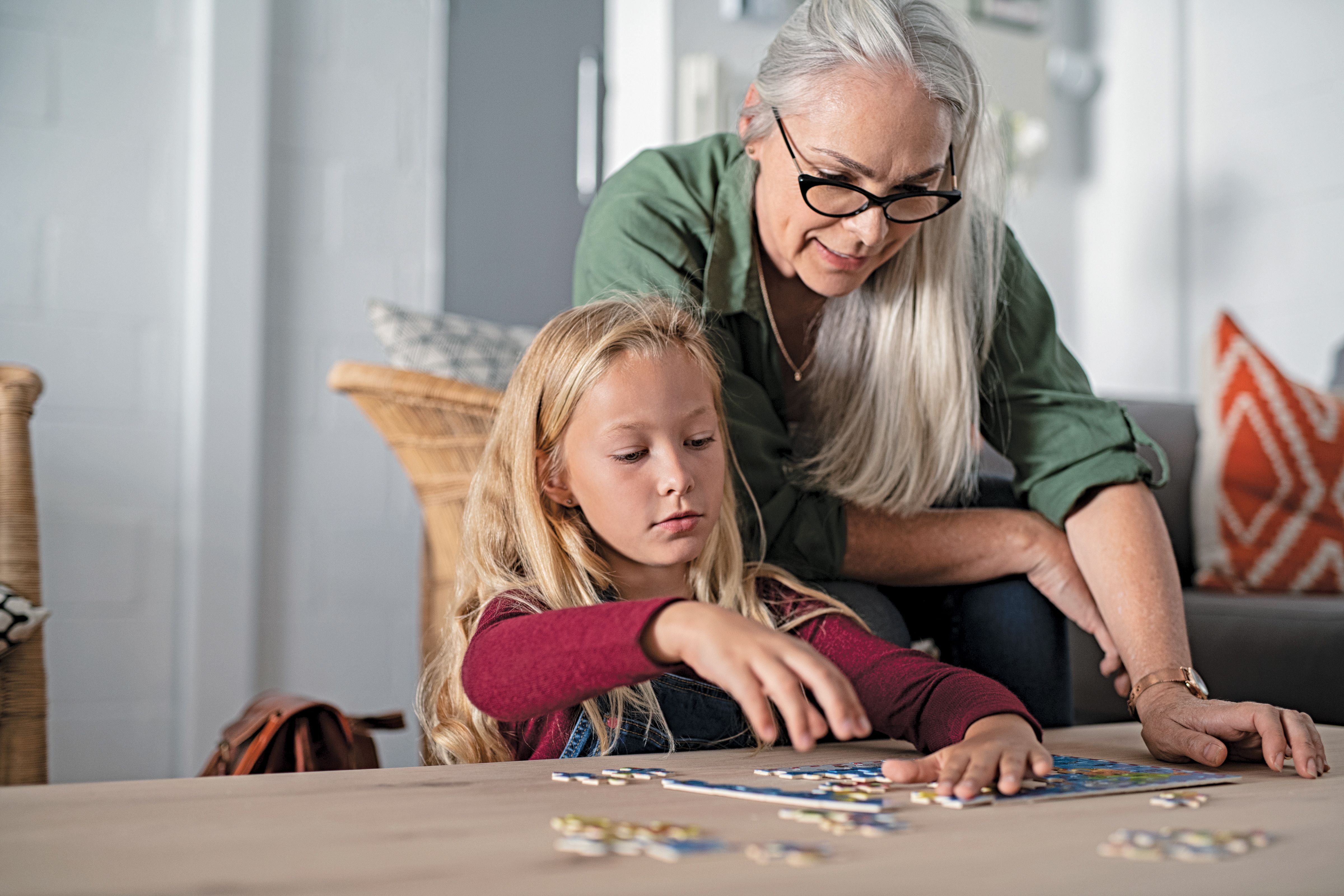 Concentrated little girl doing jigsaw puzzle with Grandmother at home. 