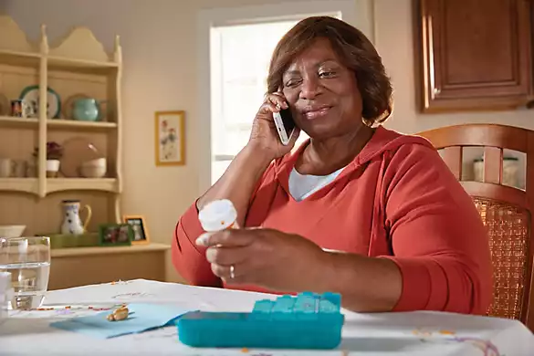 Senior woman sitting at table, reviewing medication bottle while on the phone