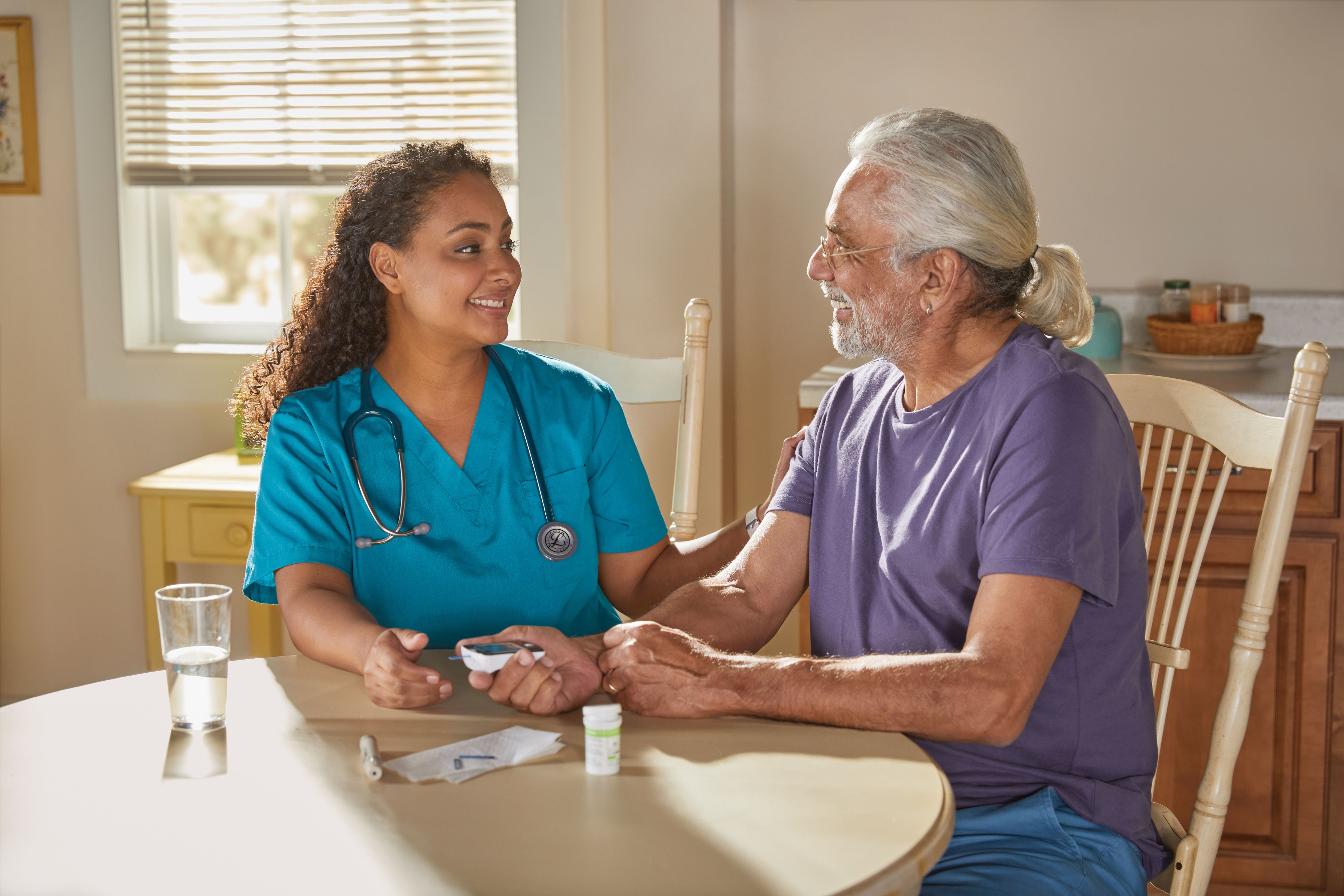 Senior man reviews using blood sugar kit with nurse at home at the table