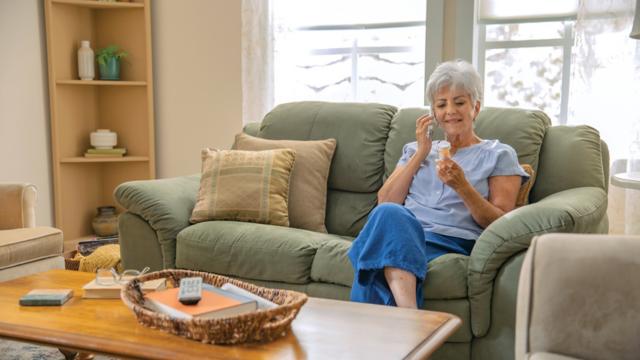 A woman uses a phone in her living room while looking at a prescription pill bottle.