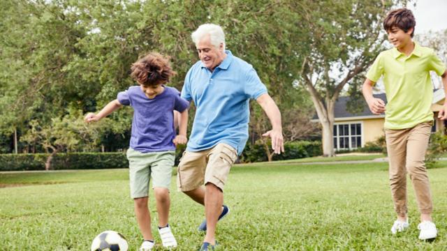 A grandfather and his grandsons play soccer outside.