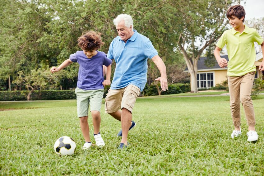 A grandfather and his grandsons play soccer outside.