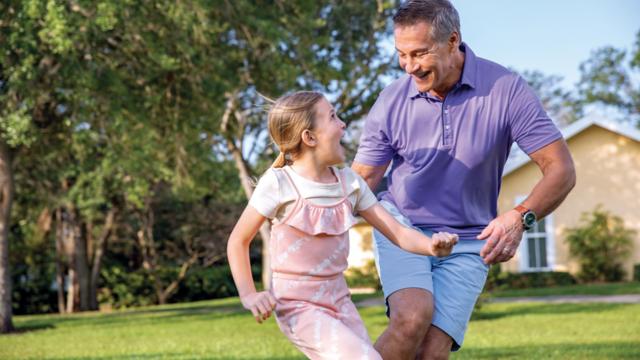 A grandfather and his granddaughter run and play outdoors.