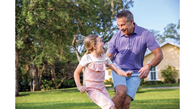 A grandfather and his granddaughter run and play outdoors.
