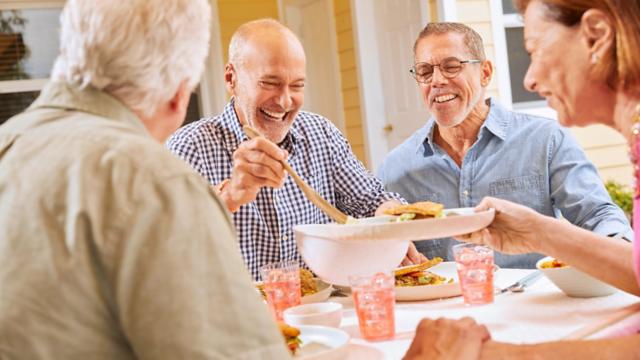 Two couples laugh and chat while sharing a meal on a patio.