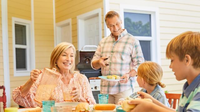 A couple smiles while enjoying lunch with their grandkids outdoors.