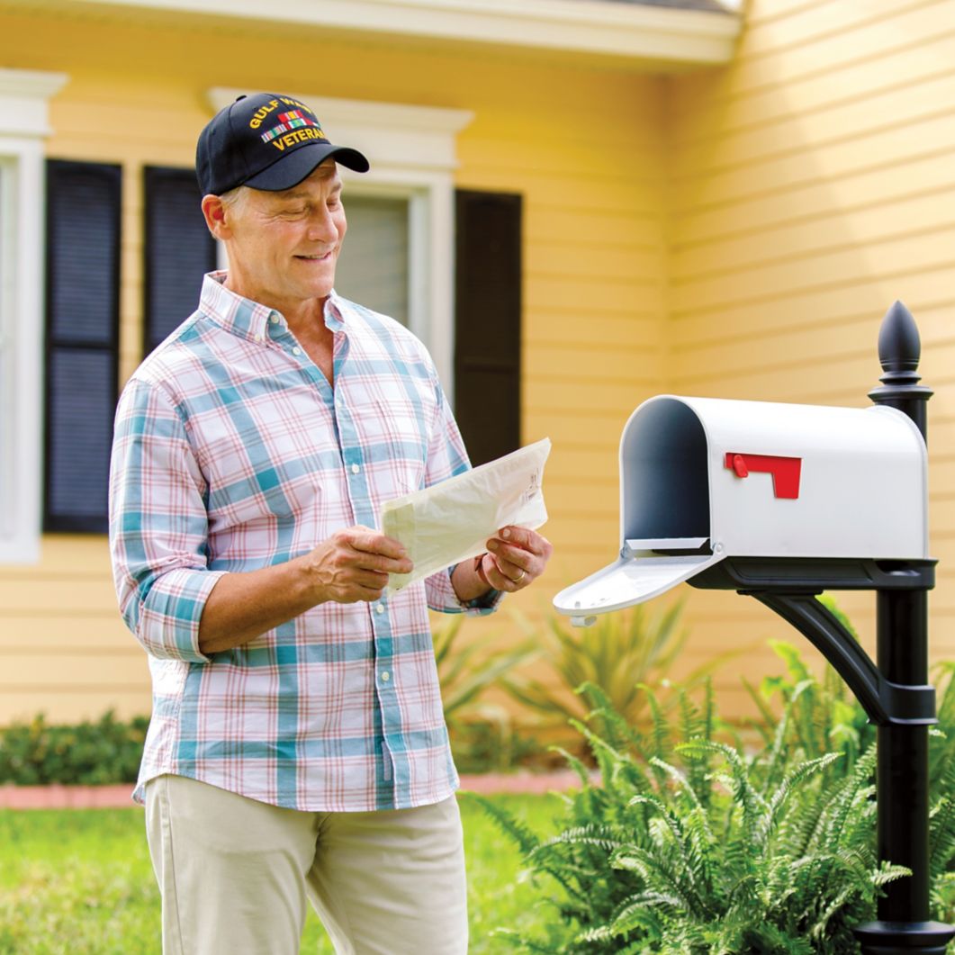 A man stands near his mailbox and smiles at a package he received.