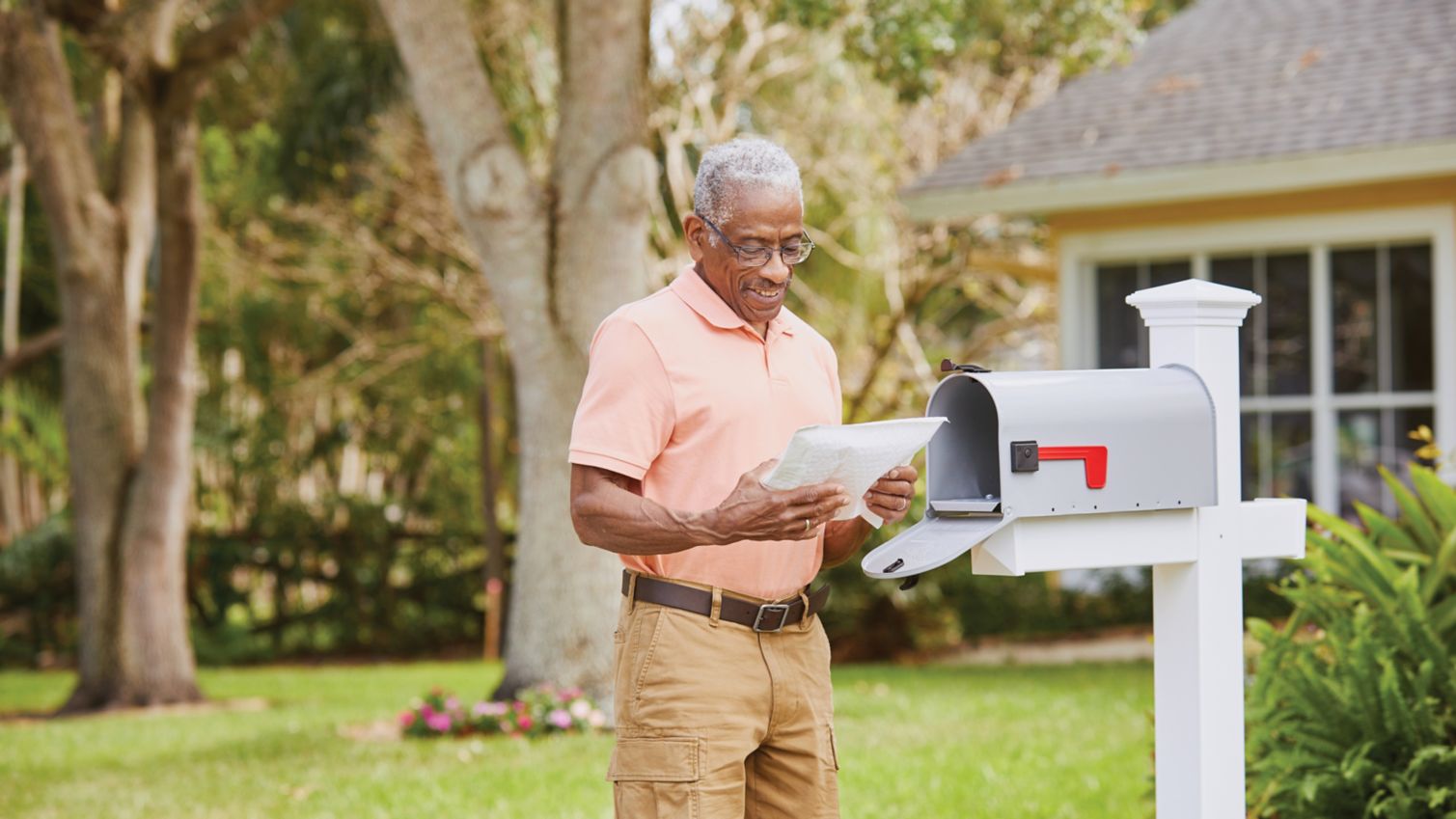 A man stands near his mailbox and smiles at a package he received.