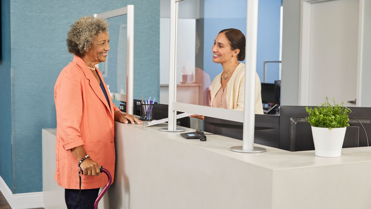 A Humana member stands at a hospital counter talking to a hospital employee about common payment terms.