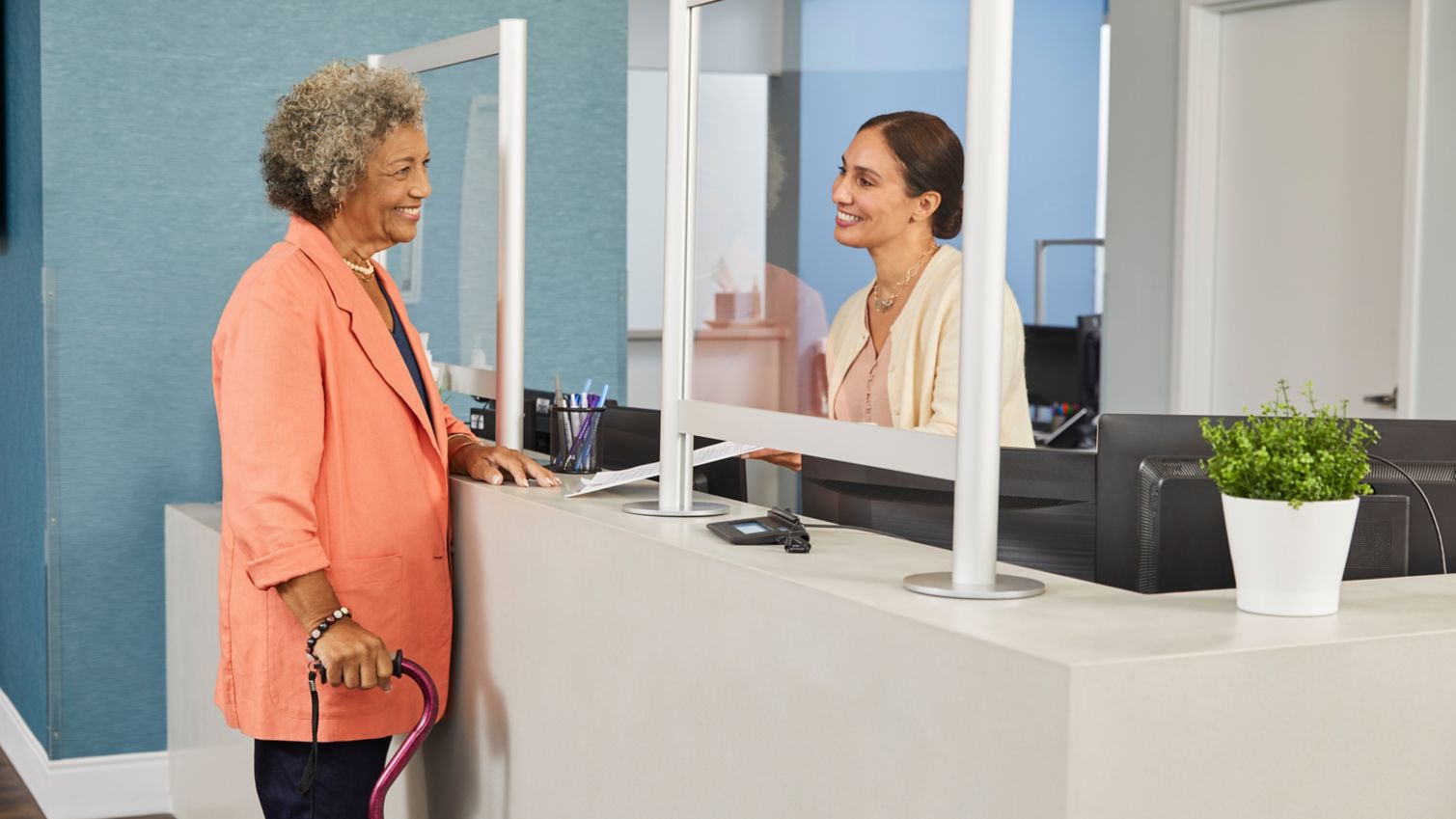Senior woman checks in with receptionist at medical office.