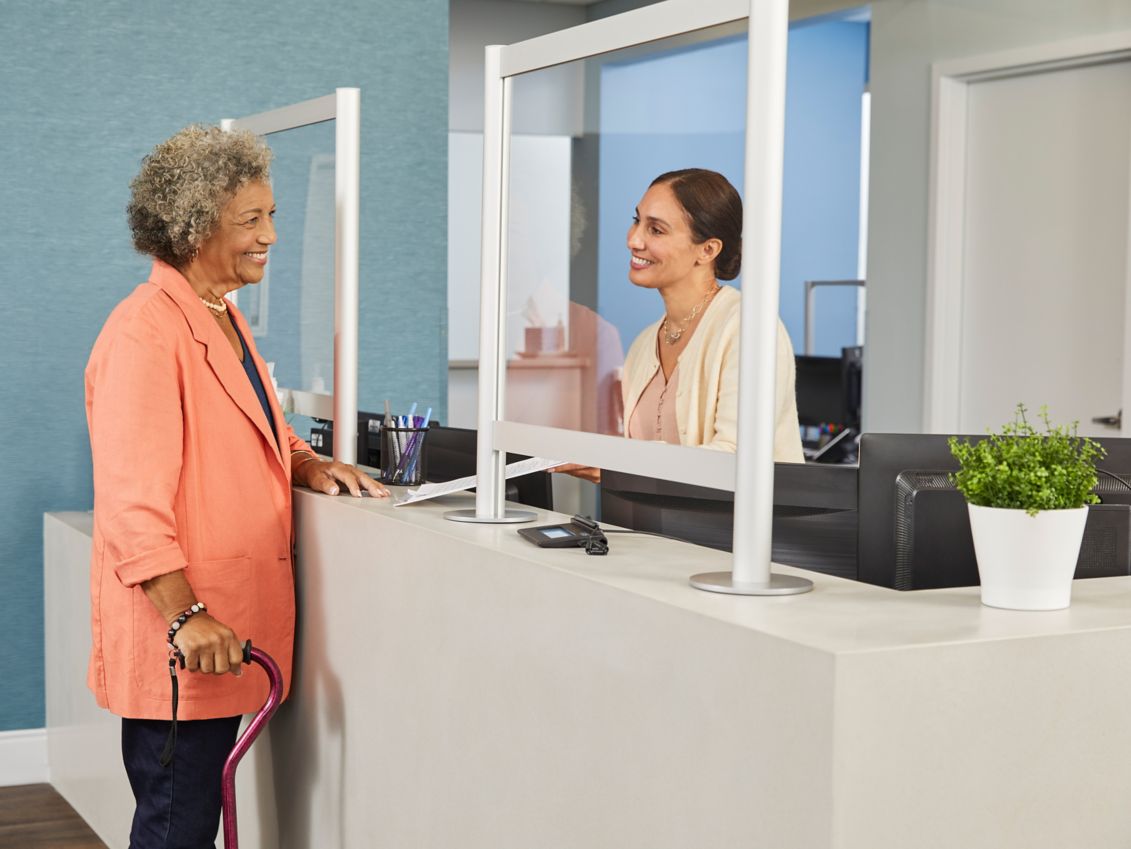 Senior woman checks in with receptionist at medical office.