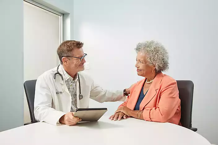 Male doctor is engaged in discussion with senior female patient, sitting at table in doctor office