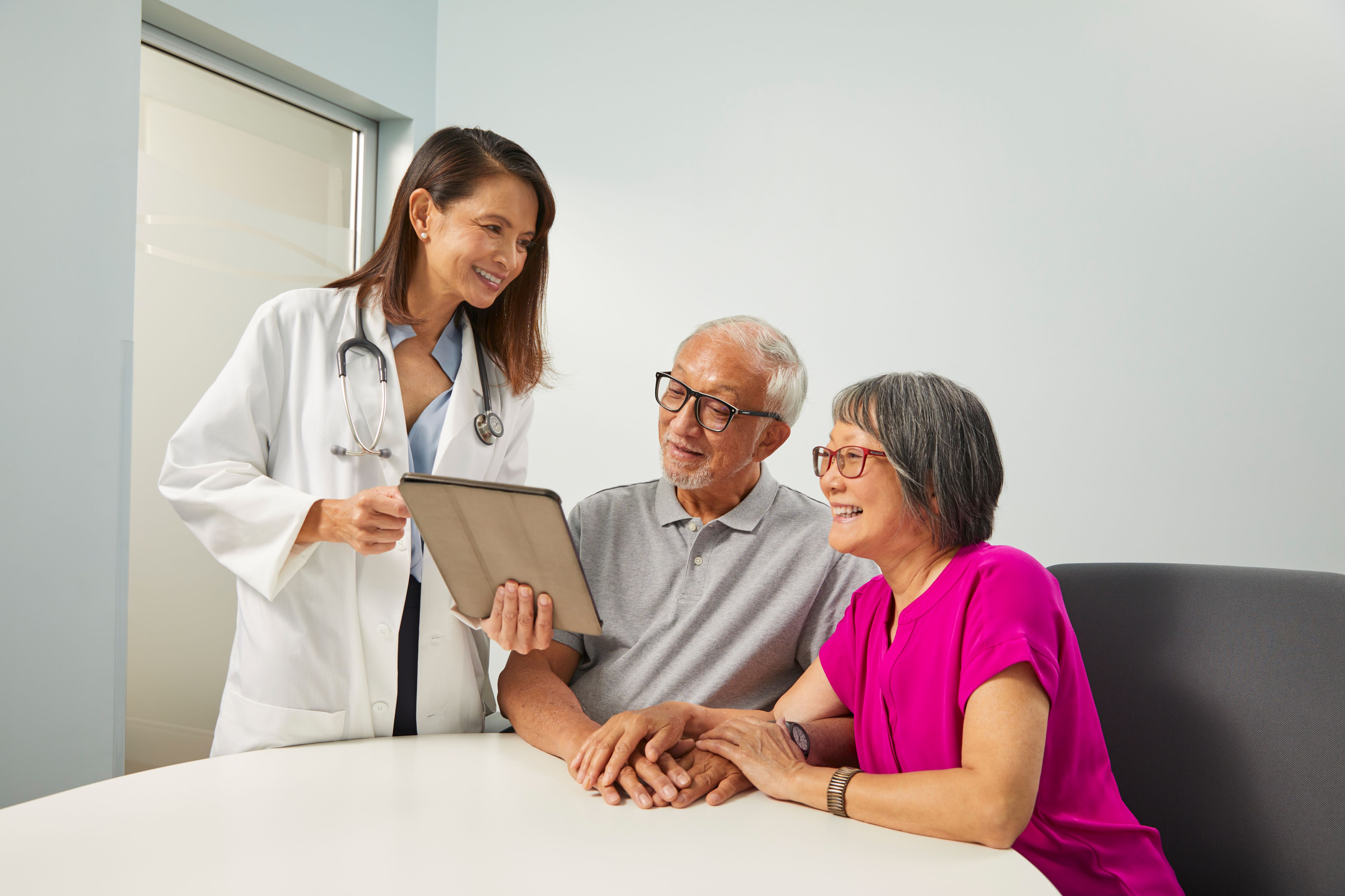 Female doctor has consultation visit with senior couple, couple is sitting at table and doctor is standing.