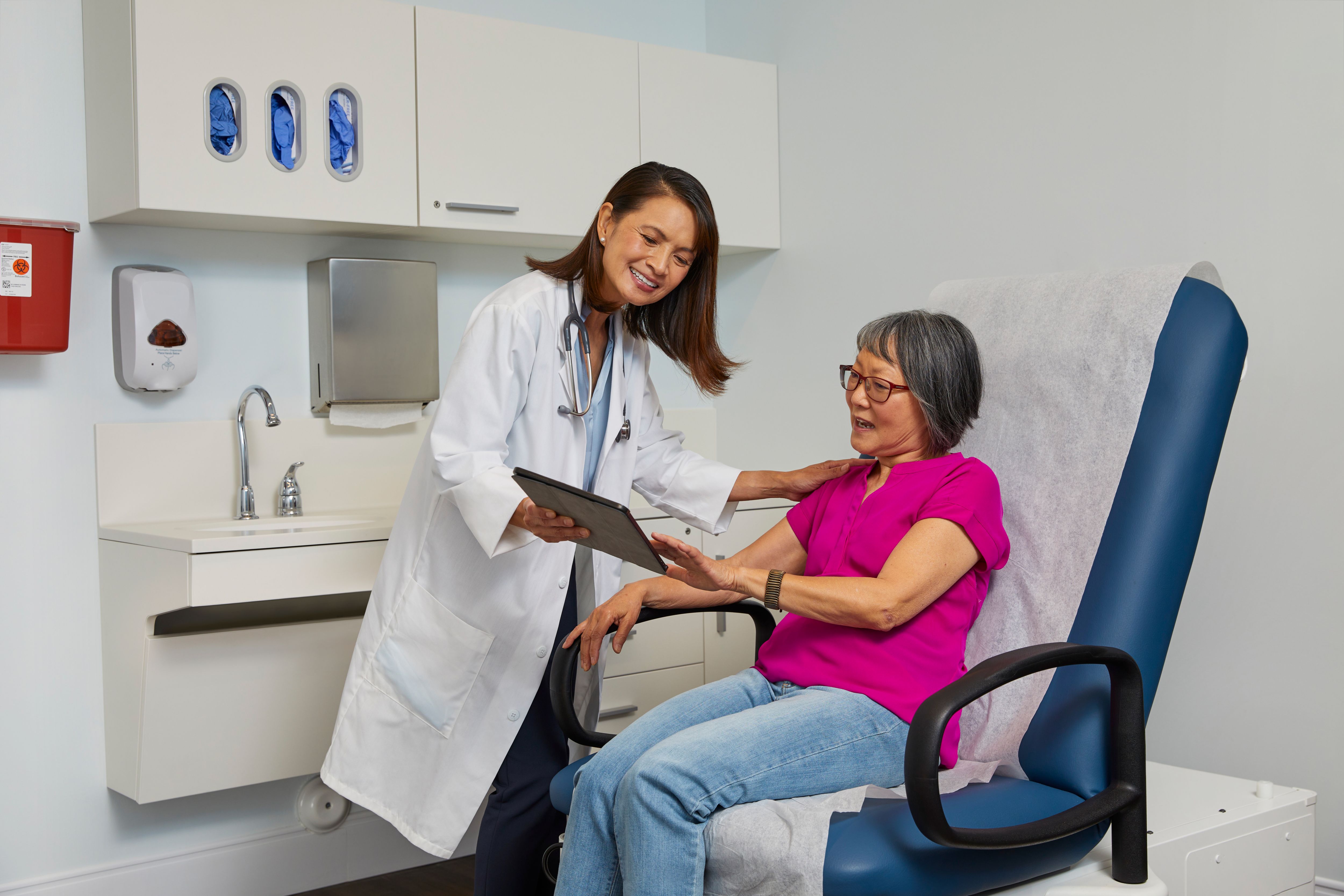 Female doctor is meeting with female patient during exam and both are looking at tablet