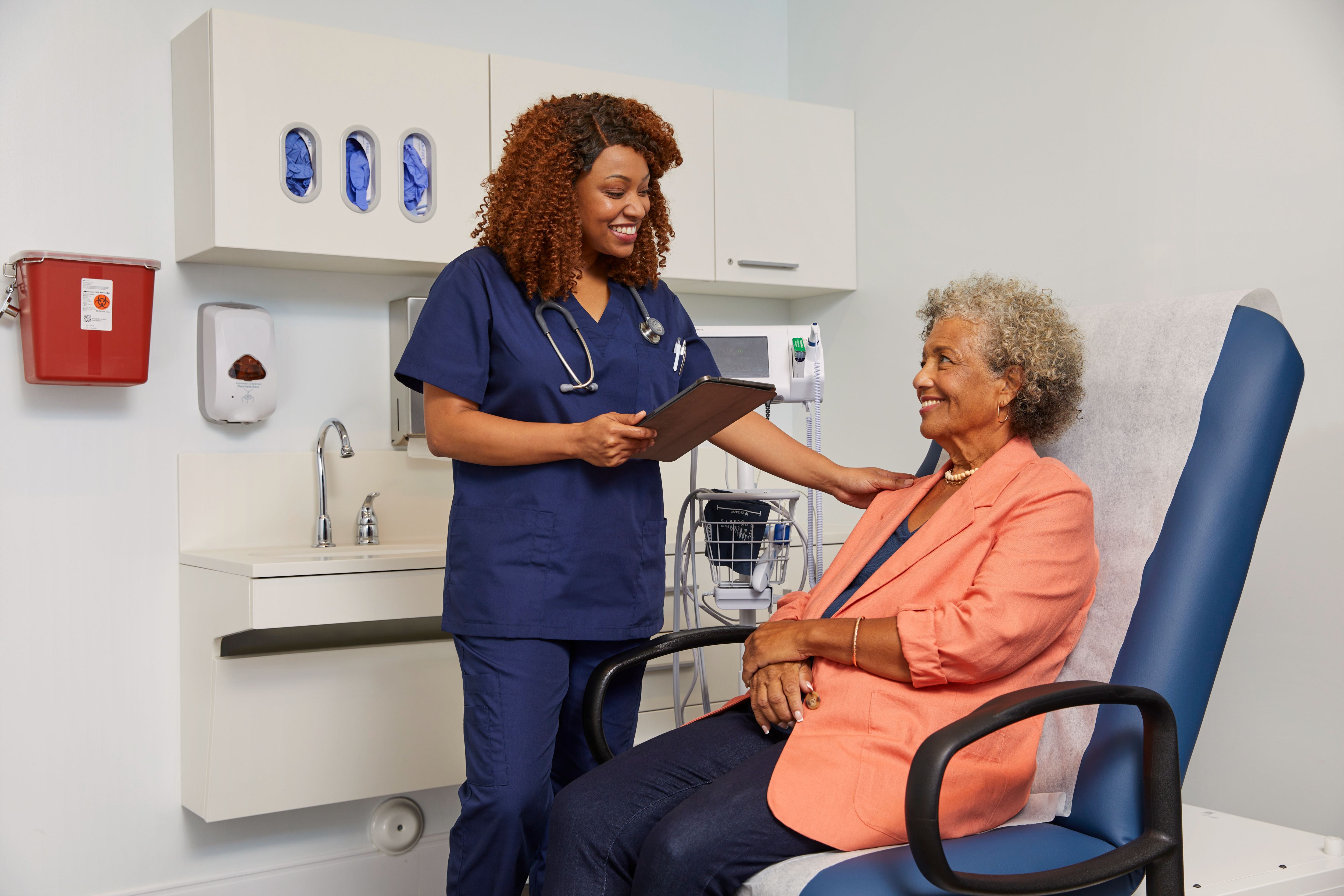 Female nurse is meeting with female patient during exam, nurse is looking at tablet