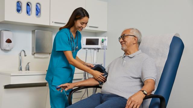 A man smiles at his nurse while she takes his blood pressure in an office.