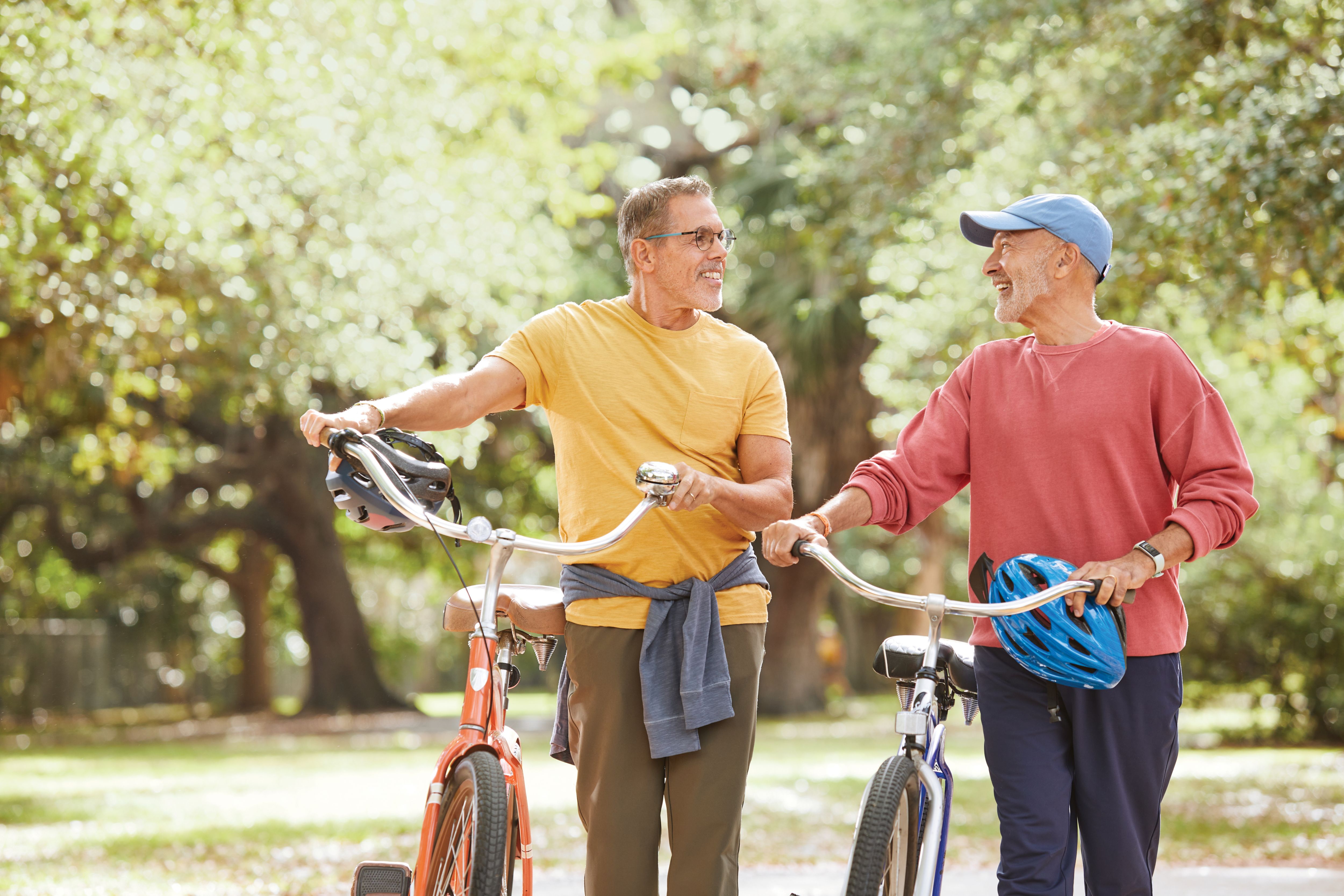 A couple smiles and chats while walking their bikes along a path in a park.