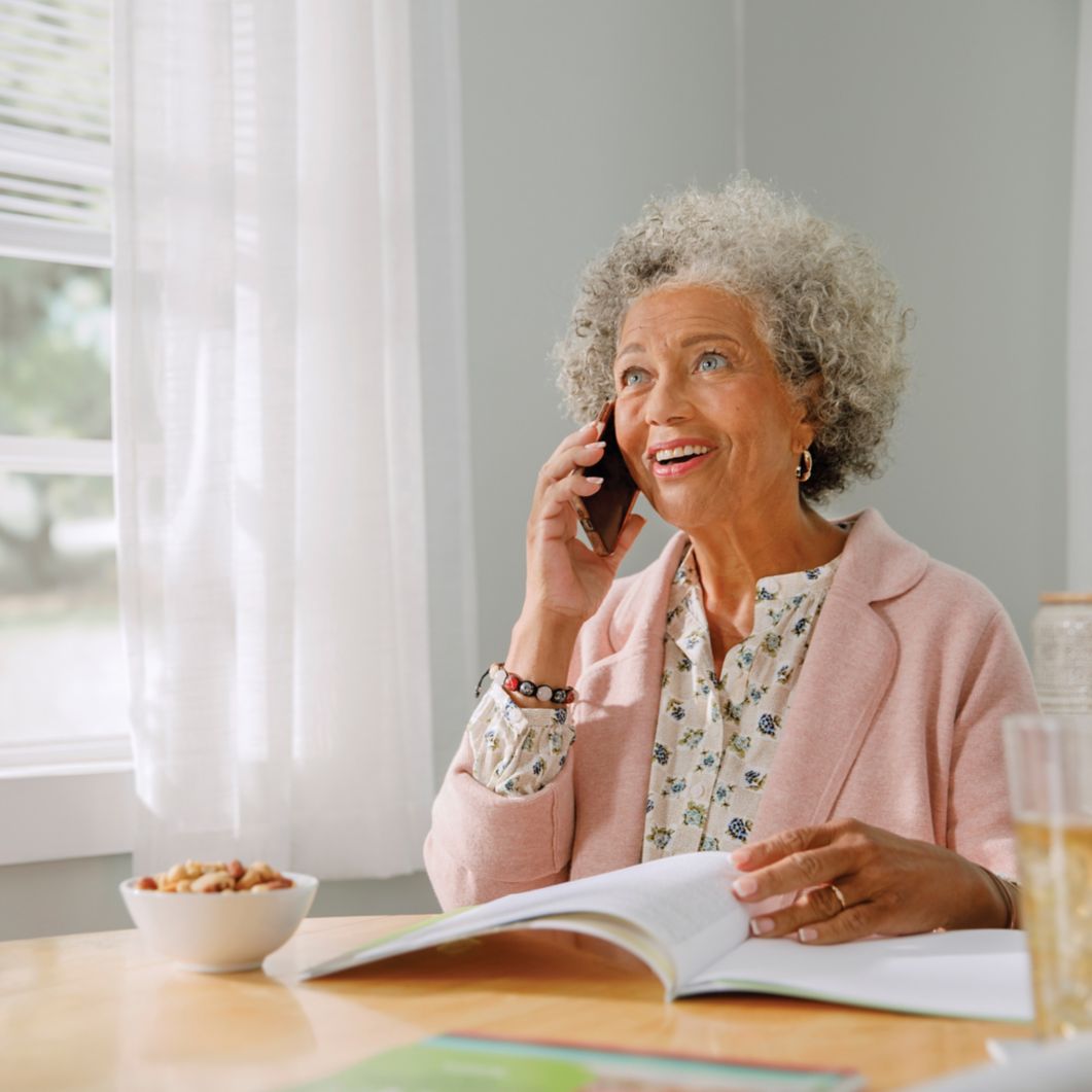 A woman makes a phone call from her home while reviewing a booklet. 