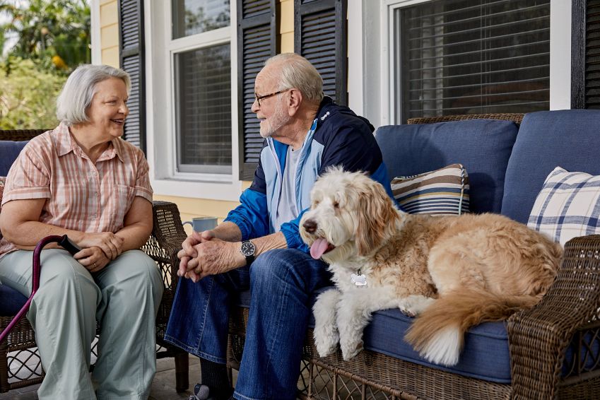 A couple relaxes on the front porch with their dog