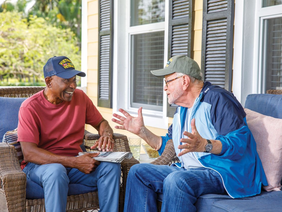 2 older male U.S. military veterans talking on a porch.