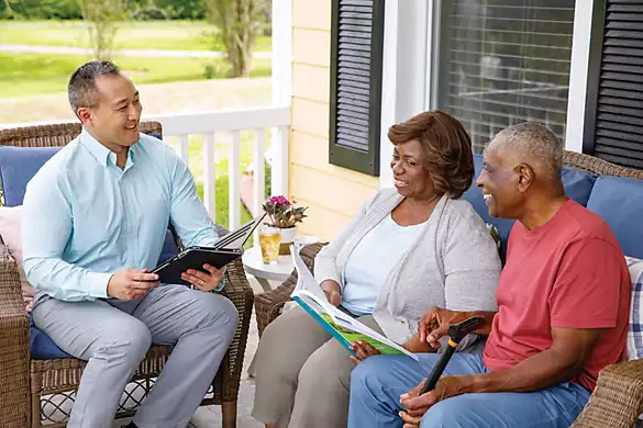 Senior couple reviews paperwork with agent together sitting on front porch