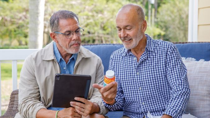 A couple sits on their porch reviewing medications and a tablet.