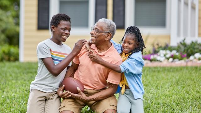 A man plays football with his grandkids in his yard. 