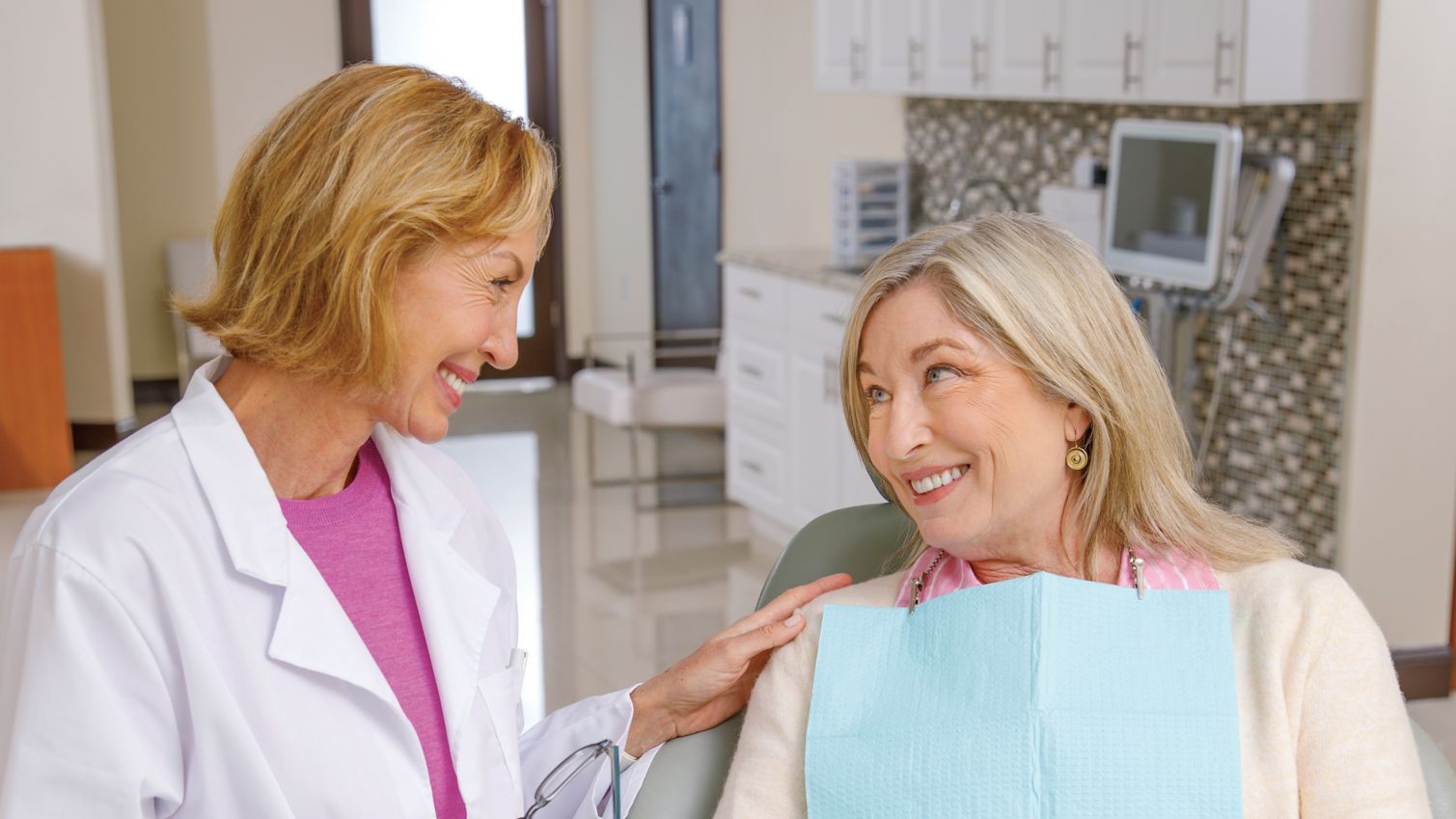 A woman smiles in her dentist's office while talking to her provider.