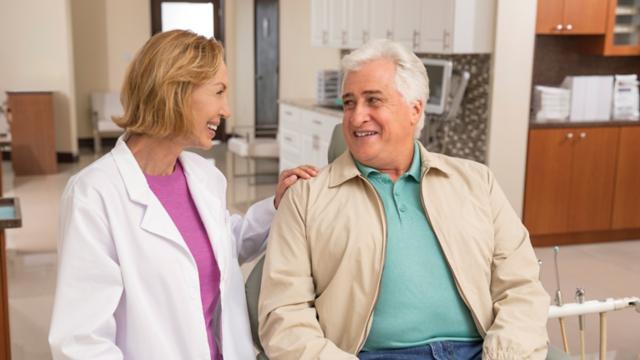 Senior man sitting in dentist chair getting ready for dental visit with female dentist