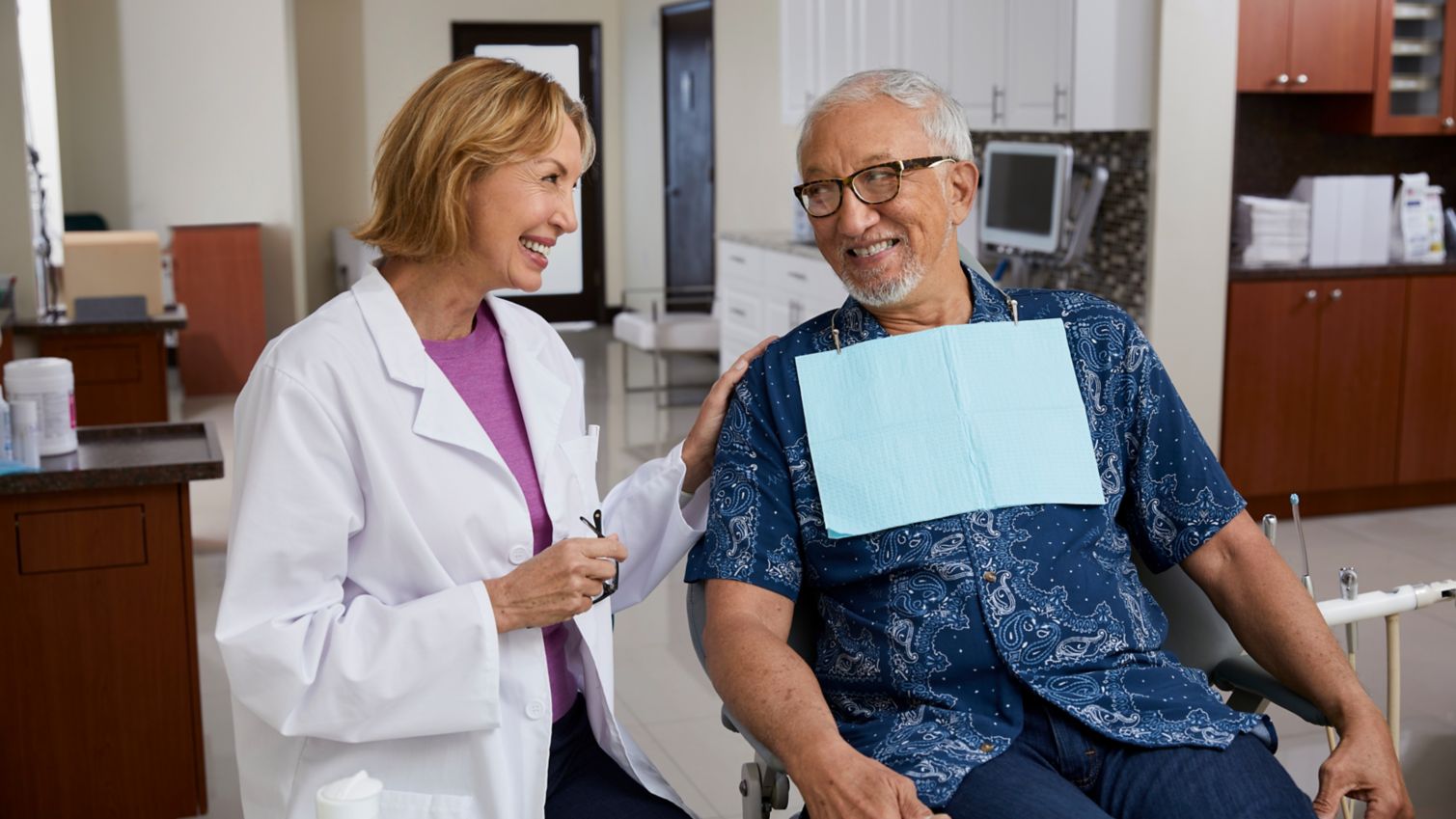 A man smiles in his dentist's office while talking to his provider.