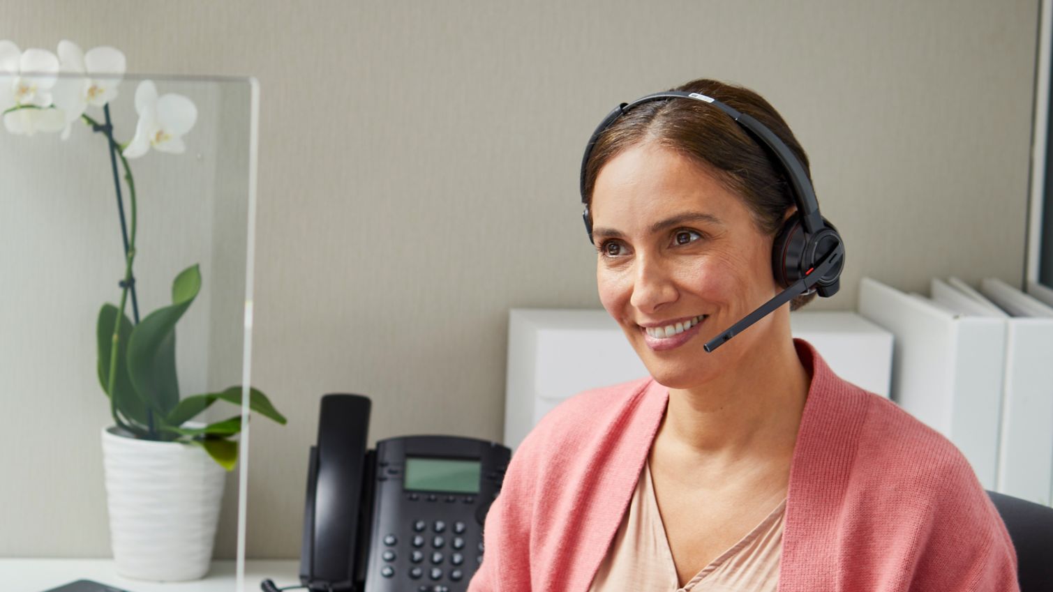 A woman in a cubicle smiles on a call with a customer. 