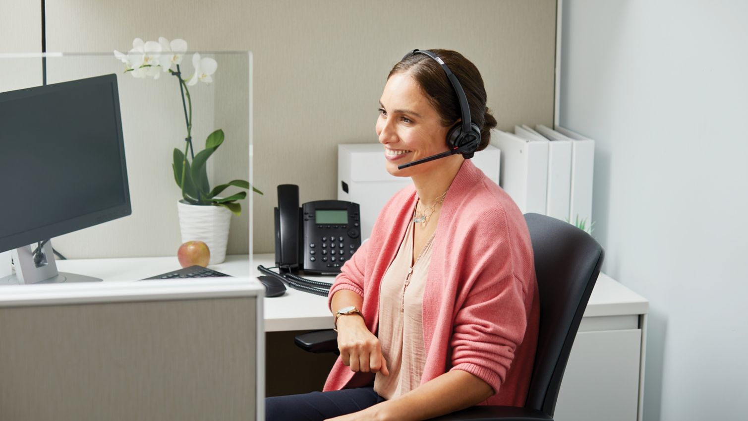 A woman in a cubicle smiles while talking to a customer on the phone.