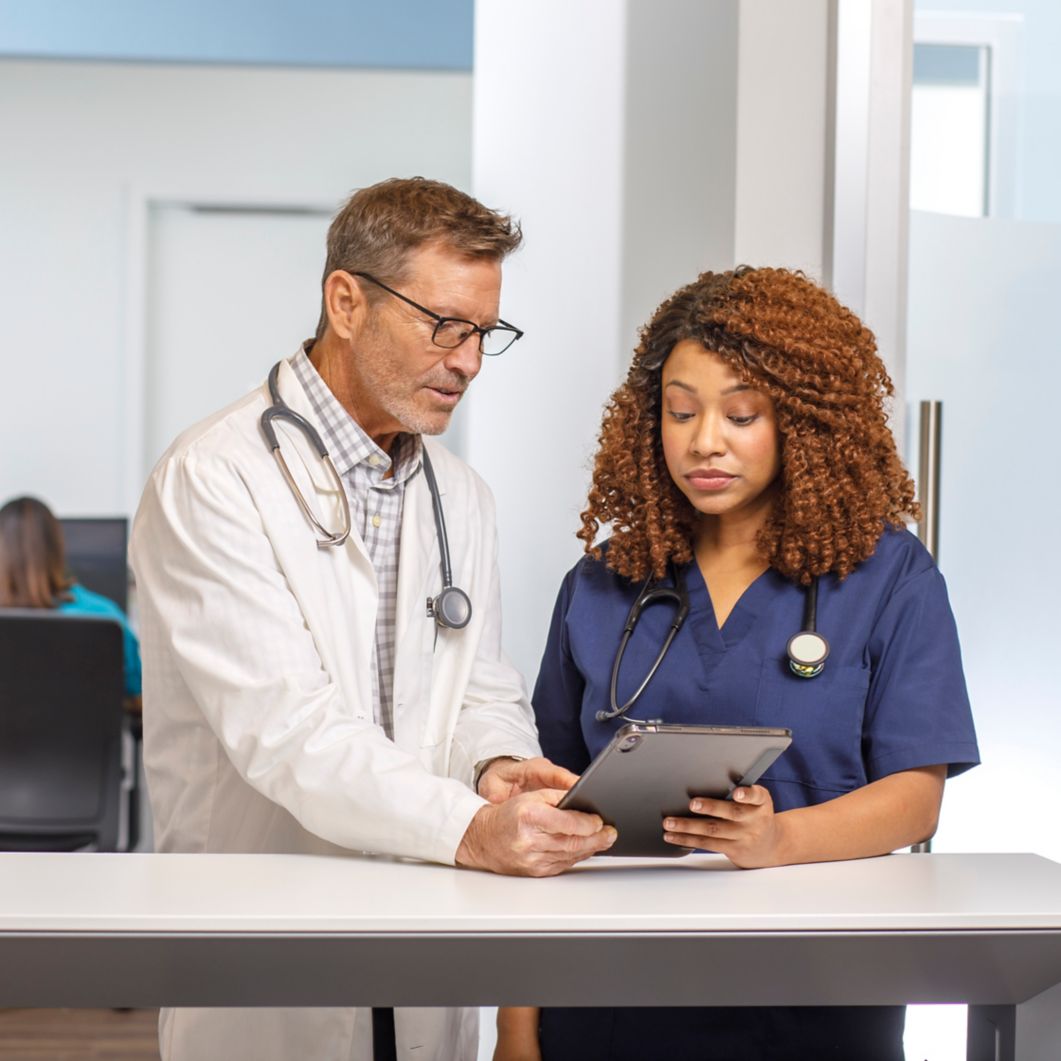 A doctor and a nurse discuss a patient’s chart seen on a tablet.